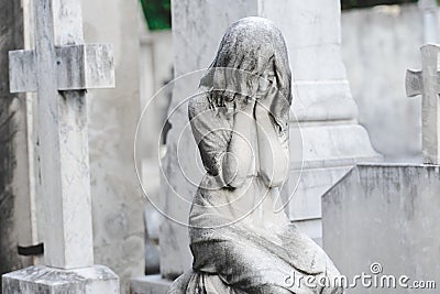 Sculpture of a angel girl in an old cemetery. Closeup of stoned angel with closed eyes and cross monument at cemetery. Graveyard Stock Photo