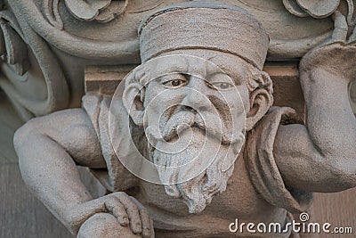 Sculpture of an old small and bearded funny man, dwarf, as an atlant in downtown of Magdeburg, Germany, closeup, details Stock Photo