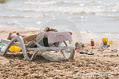 On sea beach near the water with a beach chair sunbathing girl, spanking and childrens sand toys Stock Photo