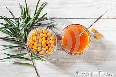 Sea buckthorn jam and fresh berries in glass jars and a green branch on a white wooden table Stock Photo