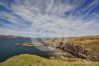 Sea cliff with low headland in the background and blue sky with white cirrus clouds Stock Photo