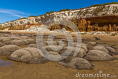 Sea eroded boulders protrude from the sand in front of the white, red and orange stratified chalk cliffs at Old Hunstanton Stock Photo