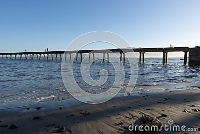 From sea level silhouettes of small figures of three people walking along long historic Wharf projecting into bay Editorial Stock Photo