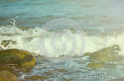 Sea surface with white wave over beach stones. Seashore under sun toned photo. Stock Photo