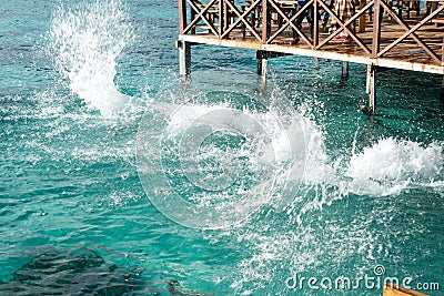 Sea water splashes after jumping to the ocean on light green ripples background in tropical warm destination next to wooden Editorial Stock Photo
