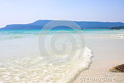 Sea wave over white sand beach. Empty seaside of tropical island with distant mountains. Stock Photo