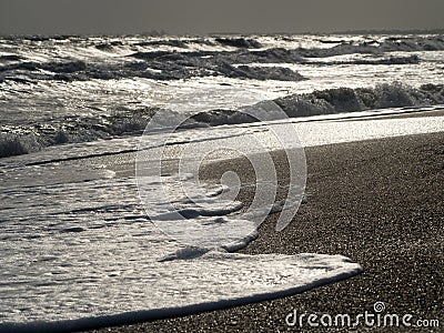 Sea waves roll over the sandy shore. The foam slides along the shore back into the sea. Stock Photo