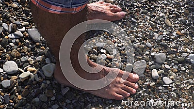 A sea waves on a stone beach covering the rocks and male feet. Media. Close up of man standing on the sea shore, summer Stock Photo