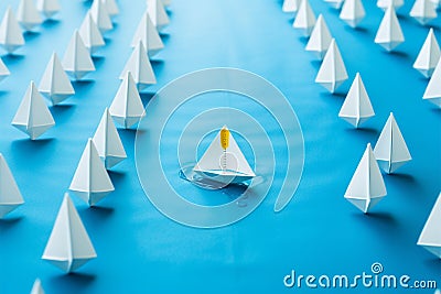 In a sea of white, a lone blue paper boat leads Stock Photo