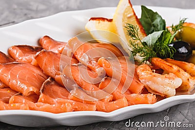 Seafood platter with salmon slice, shrimp, slices fish fillet, decorated with olives and lemon in plate over rustic background. Stock Photo