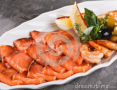 Seafood platter with salmon slice, shrimp, slices fish fillet, decorated with olives and lemon in plate over rustic background. Stock Photo