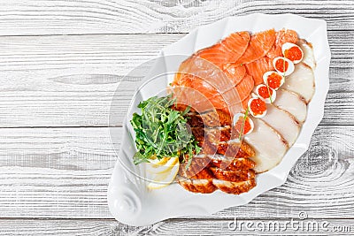 Seafood platter with salmon slice, smoke sturgeon, quail eggs with red caviar, slices fish fillet with arugula on wood background Stock Photo