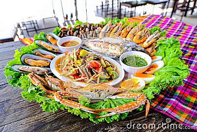 Seafood Somtum has clams, shrimp, crabs, boiled eggs, grilled tilapia, placed in a beautifully placed tray on wooden table Stock Photo