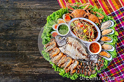 Seafood Somtum has clams shrimp, crabs, boiled eggs, grilled tilapia, placed in a beautifully placed tray on a wooden table Stock Photo