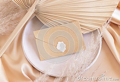 Sealed envelope on plate on dried palm leaf and beige silky fabric close up, mockup Stock Photo