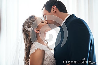 Sealed with a kiss. an affectionate young couple standing indoors together and kissing after their wedding. Stock Photo