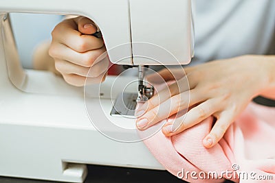 Seamstress works on a sewing machine. The girl sews and holds a pink cloth Stock Photo