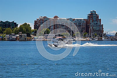 Seaplane landing on water with a port and buildings in the background under a blue sky in Canada Editorial Stock Photo