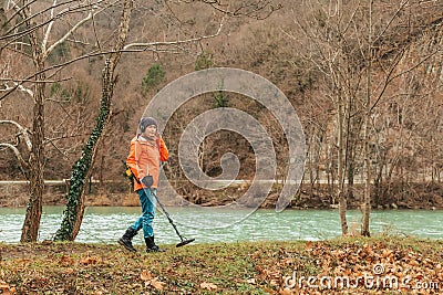 Search With A Metal Detector. A young woman in an orange jacket is looking for lost artifacts along the river. Copy space Stock Photo