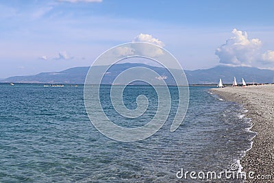 Seascape on a hot summer day, clear calm blue sea, clear sky, pebble beach, catamarans with sails and kayaks on the horizon, outdo Stock Photo