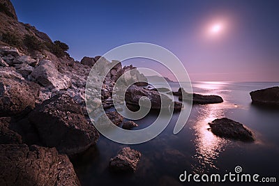 Seascape with moon and lunar path with rocks at night Stock Photo