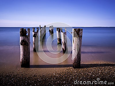 Seascape with pilings of ruined piers and resting cormorants on tropical beach Stock Photo