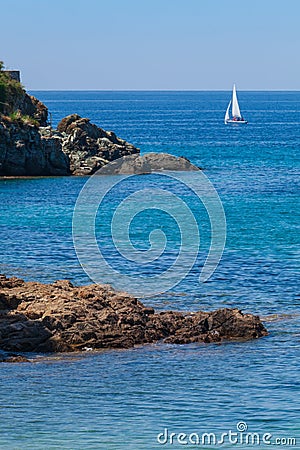 Seashore coastline with cliff and rocks on a mountain slope. Blue sea and a a sailboat in the background. Island of Elba in Italy Stock Photo