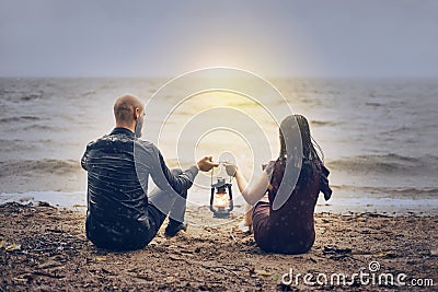 On the seashore a young couple guy and girl at sunset. man and woman hold flashlight in hands together Stock Photo