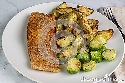 seasoned baked salmon with potato wedges and roasted brussel sprouts Stock Photo