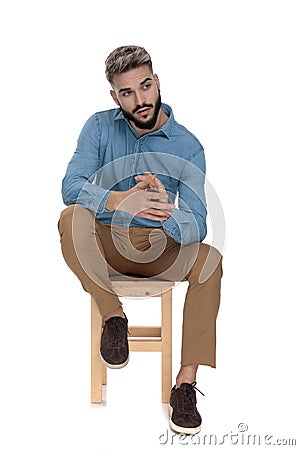 Seated charmed man looking away while rubbing his palms Stock Photo