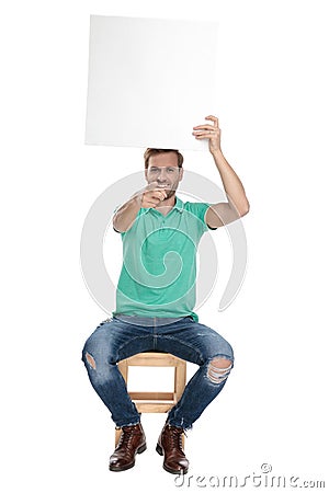 Seated man pointing finger to camera while holding empty board Stock Photo