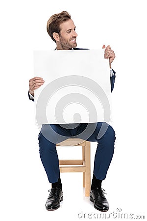 Seated fashion guy holds blank carton board while looking away Stock Photo