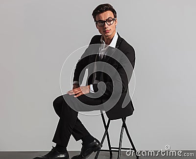 Seated man in tuxedo and undone bowtie looks to side Stock Photo