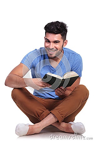 Seated young casual man reading a book and smiles Stock Photo