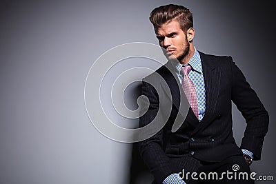 Seated young fashion model in suit looks away Stock Photo
