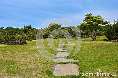 Secluded area with rocky steps, grass, and trees with blue sky in Camellia Hill of Jeju Island, South Korea. Stock Photo