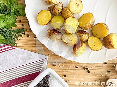 second courses, baked potatoes cooked in a rustic way, in a white plate on a wooden table with herbs, mushrooms and spices, view f Stock Photo