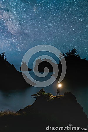 Secret Beach Oregon at Night with Stars and hiker Standing with the Light Stock Photo