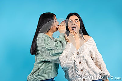 Secrets and emotion. Smiling twin women wearing fashion clothes on blue background with empty space Stock Photo