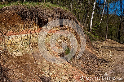 Section of a part of a slope with layers of variegated clay covered with a layer of soil on top Stock Photo