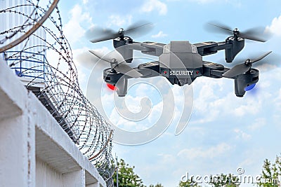 Security drone patrols the territory across the sky. Guarding the wall with barbed wire drone with blue and red beacon Stock Photo