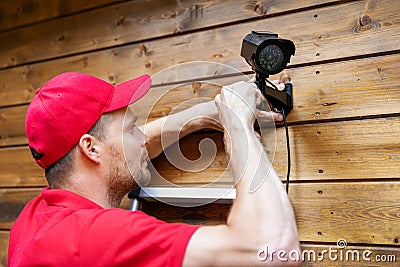 Security system technician installing surveillance camera on wooden house wall Stock Photo
