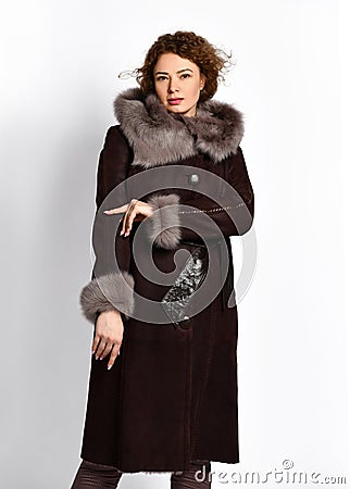Sexy red-haired curly woman in black sheepskin coat with fur hood and wide leather belt on white Stock Photo