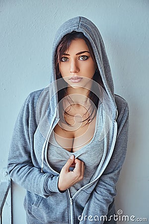 Seductive young adult brunette woman wearing a gray hoodie posing in front of a wall outdoors Stock Photo