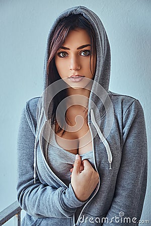 Seductive young adult brunette woman wearing a gray hoodie posing in front of a wall outdoors Stock Photo