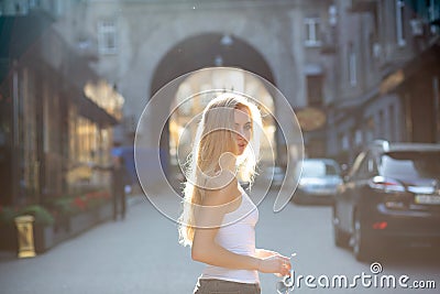 Seductive young model with long hair holding glasses, posing at the passage in rays of sun. Copy space Stock Photo