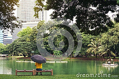 Seen from behind.Young woman with umbrella sitting near the pond in Lumpini park and Look forward . Sad and lonely Stock Photo