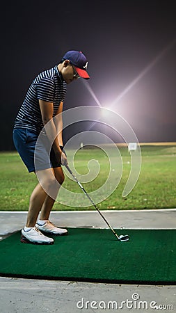 A man with a short pants swinging golf clubs at the driving range during the night Editorial Stock Photo