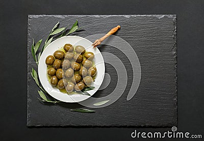 Selected olives in a white plate decorated with natural olive tree branches on a dark background. Stock Photo