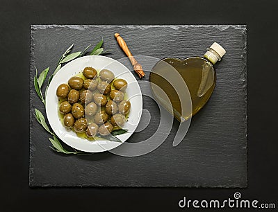 Selected olives in a white plate decorated with natural olive tree branches and olive oil heart bottle. Stock Photo